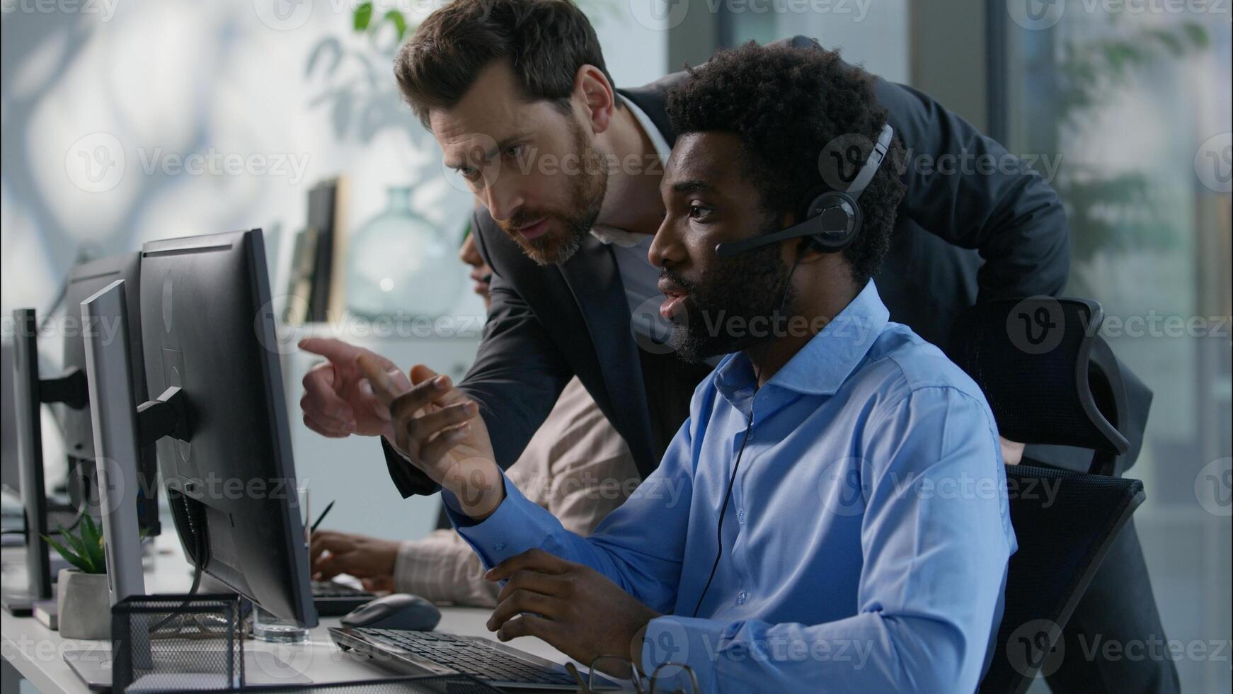 Diverse callcenter collaboration Caucasian boss explaining task pointing finger African operator headset Indian female work computer business call center customer support office communication training photo