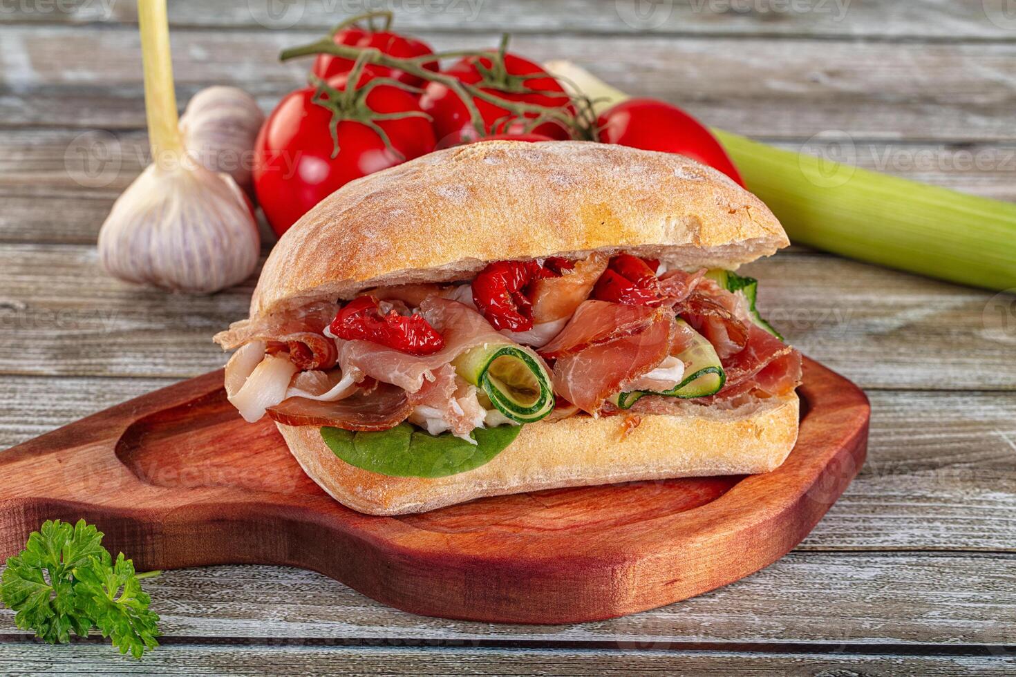A sandwich on a wooden cutting board with vegetables photo