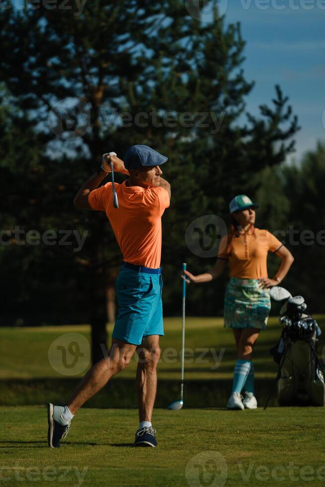 A man hits a ball on a golf course. A couple enjoys a sunny day playing golf on a bright green course photo