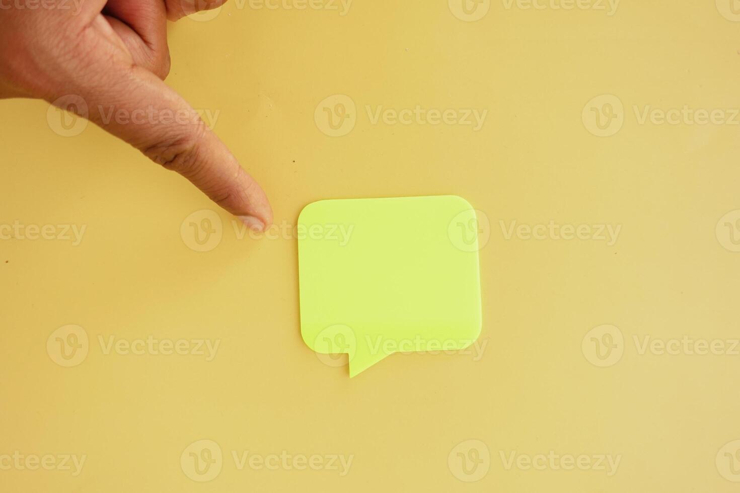 Hand pointing at green sticky note on yellow background photo