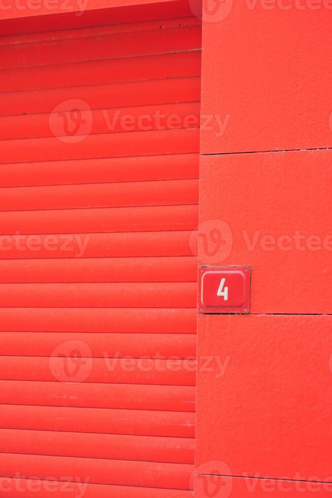 Bright red wall with closed rolling door and number label photo