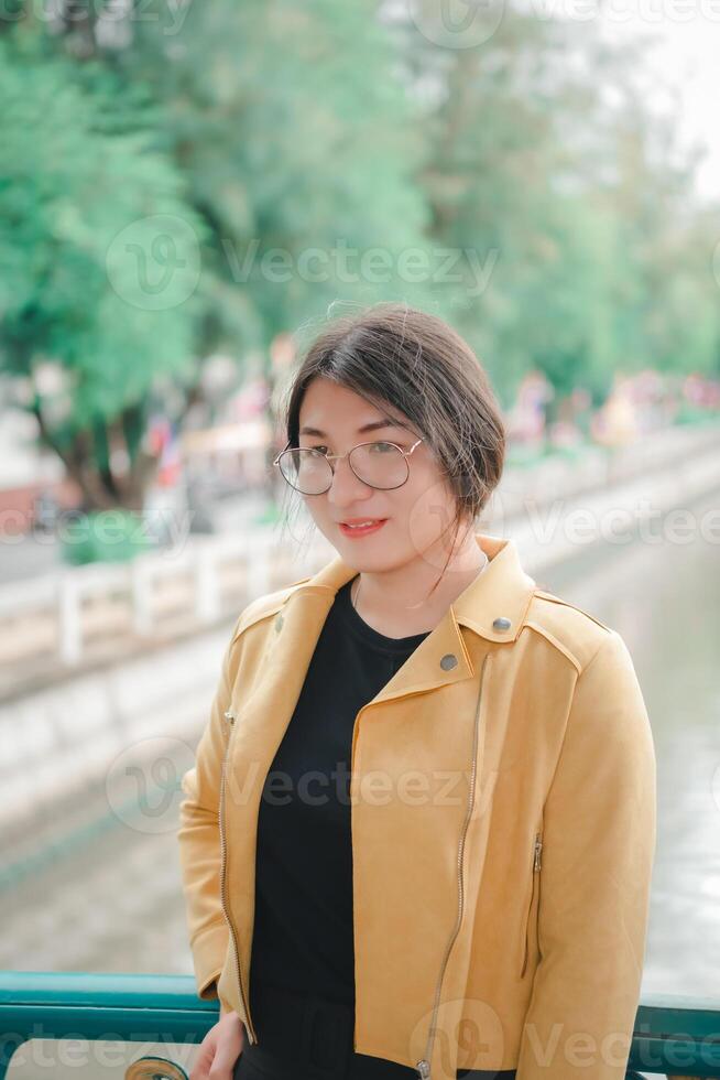 A woman wearing glasses and a yellow jacket standing on a bridge photo