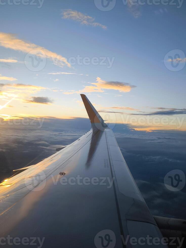 Wing of an airplane flying above clouds against the backdrop of a sunset. Flight on an airplane. photo