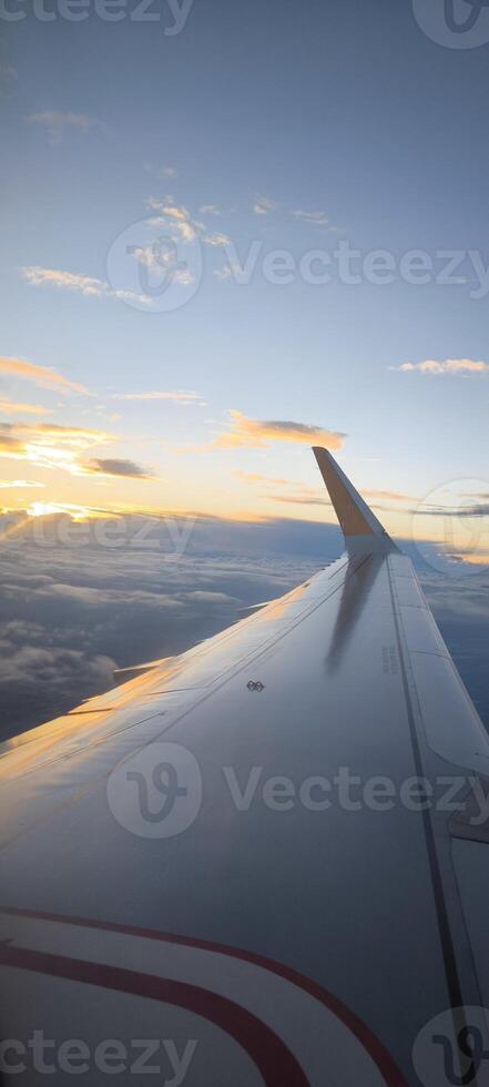 Wing of an airplane flying above clouds against the backdrop of a sunset. View from the airplane window. photo