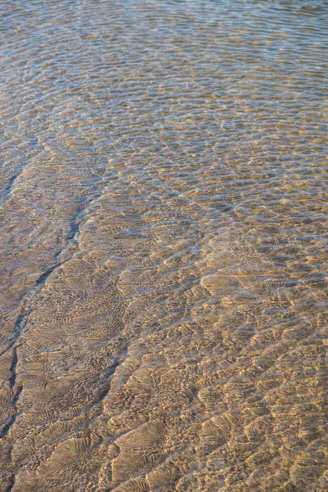close view of water edge meeting sandy beach light reflections on the surface of shallow water photo