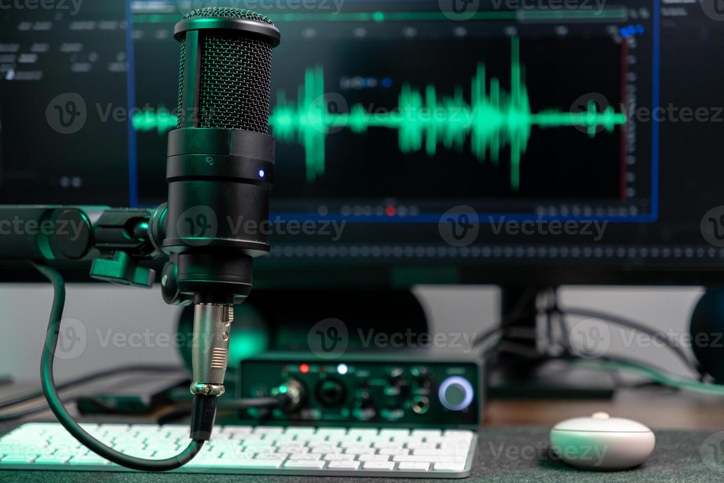 Black studio microphone with glowing green audio wave visualizer on computer monitor, representing professional podcasting, voice recording, and sound engineering photo