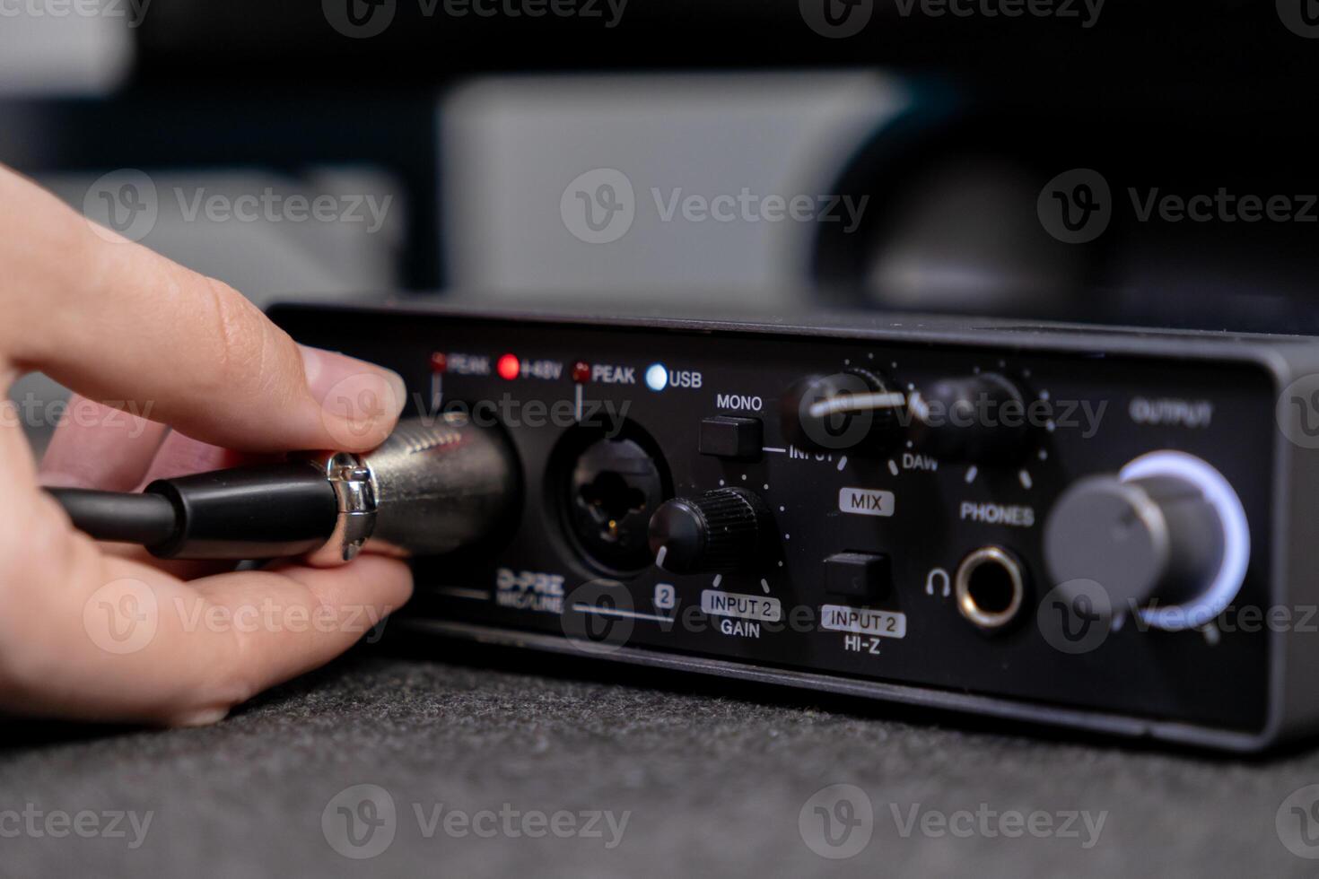 Close-up of a hand inserting an XLR microphone cable into a professional audio interface, highlighting input gain and USB indicators for home studio recording photo