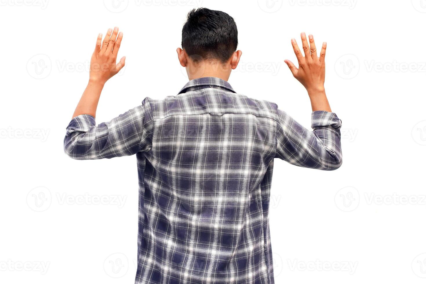 Rear view of a young Asian man with hands raised in surrender on white background. Depicting surrender photo
