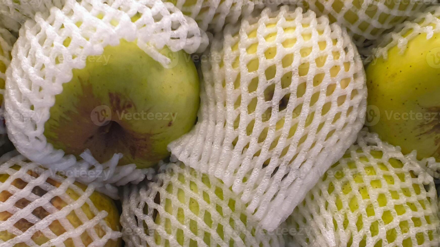 Close-up of Green Apples in Protective Netting at a Supermarket, Ready for Purchase photo
