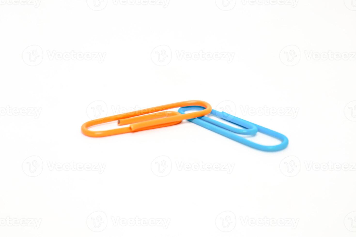 Two colorful paper clips, one orange and one blue, intertwined on white surface, minimal photo