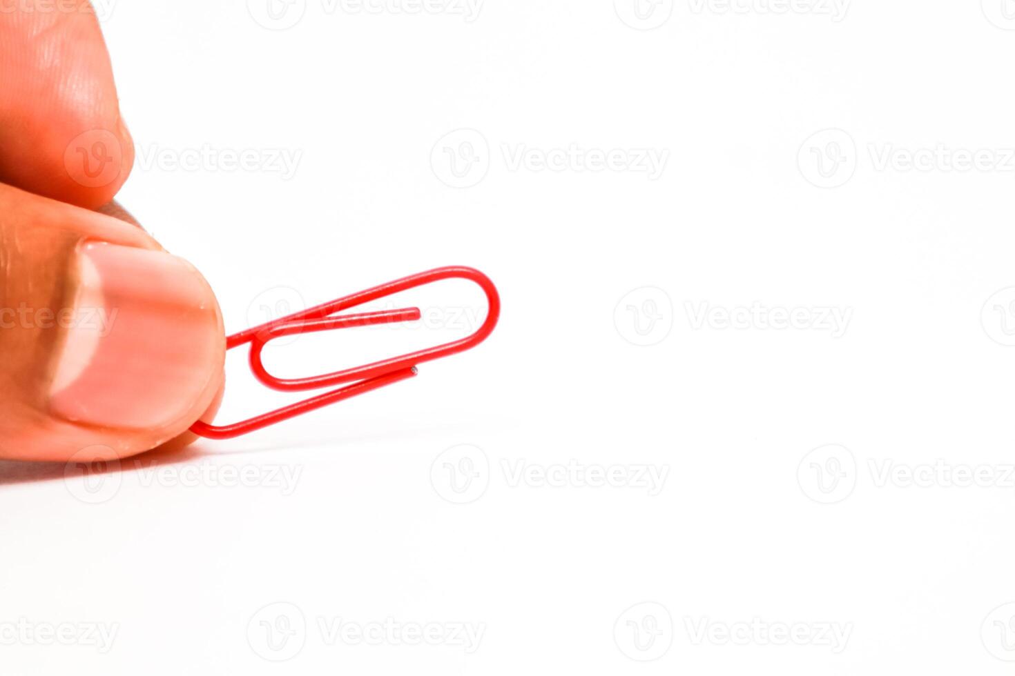 Close-up of a person's fingers holding a red paper clip against a white background photo