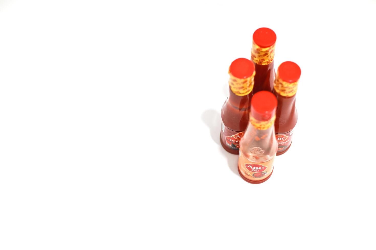 Lampung, July 03, 2025, A cluster of red-capped chili sauce bottles arranged on a plain white surface, isolated shot photo