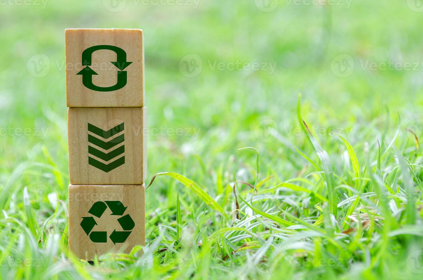 Wooden cube stack with recycle, reuse, reduce icons on green grass. Environmental concept. photo