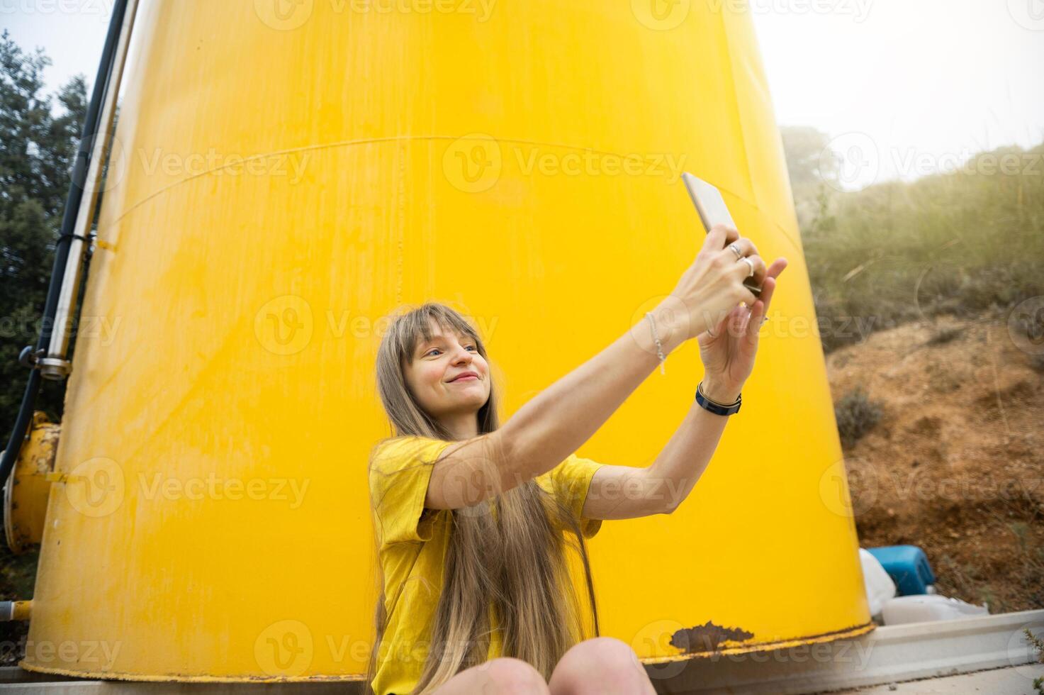 Woman Taking a Selfie in Front of a Bright Yellow Tank in a Natural Setting photo