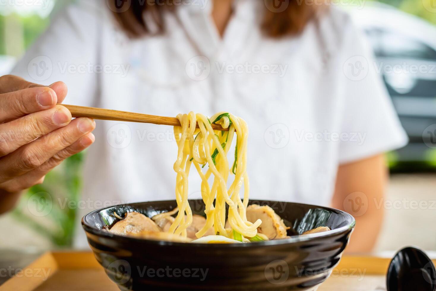 Woman eating a ramen Japanese noodle soup in a black color ramen bowl. photo