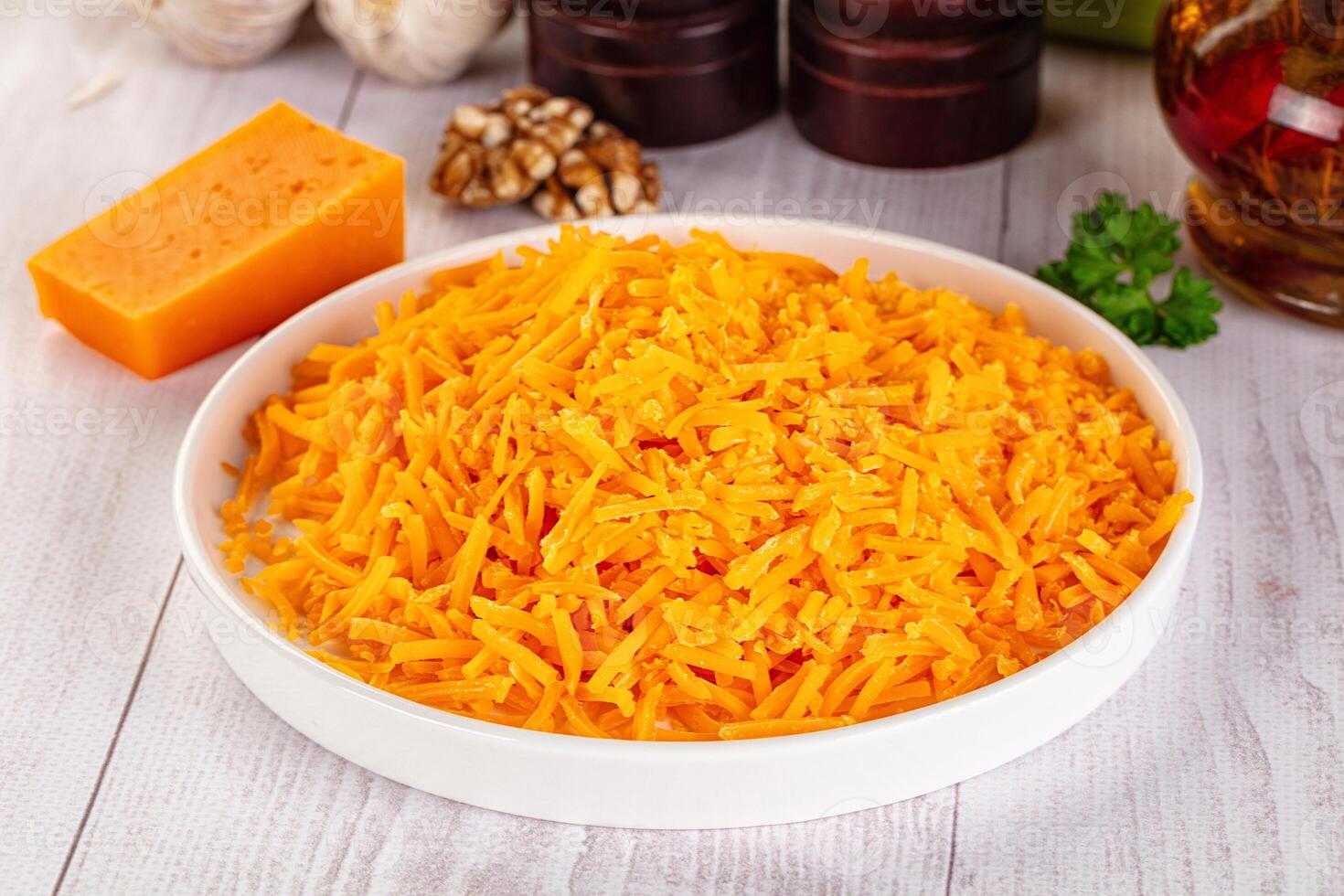 A bowl of shredded cheese on a table next to a bottle of butter photo