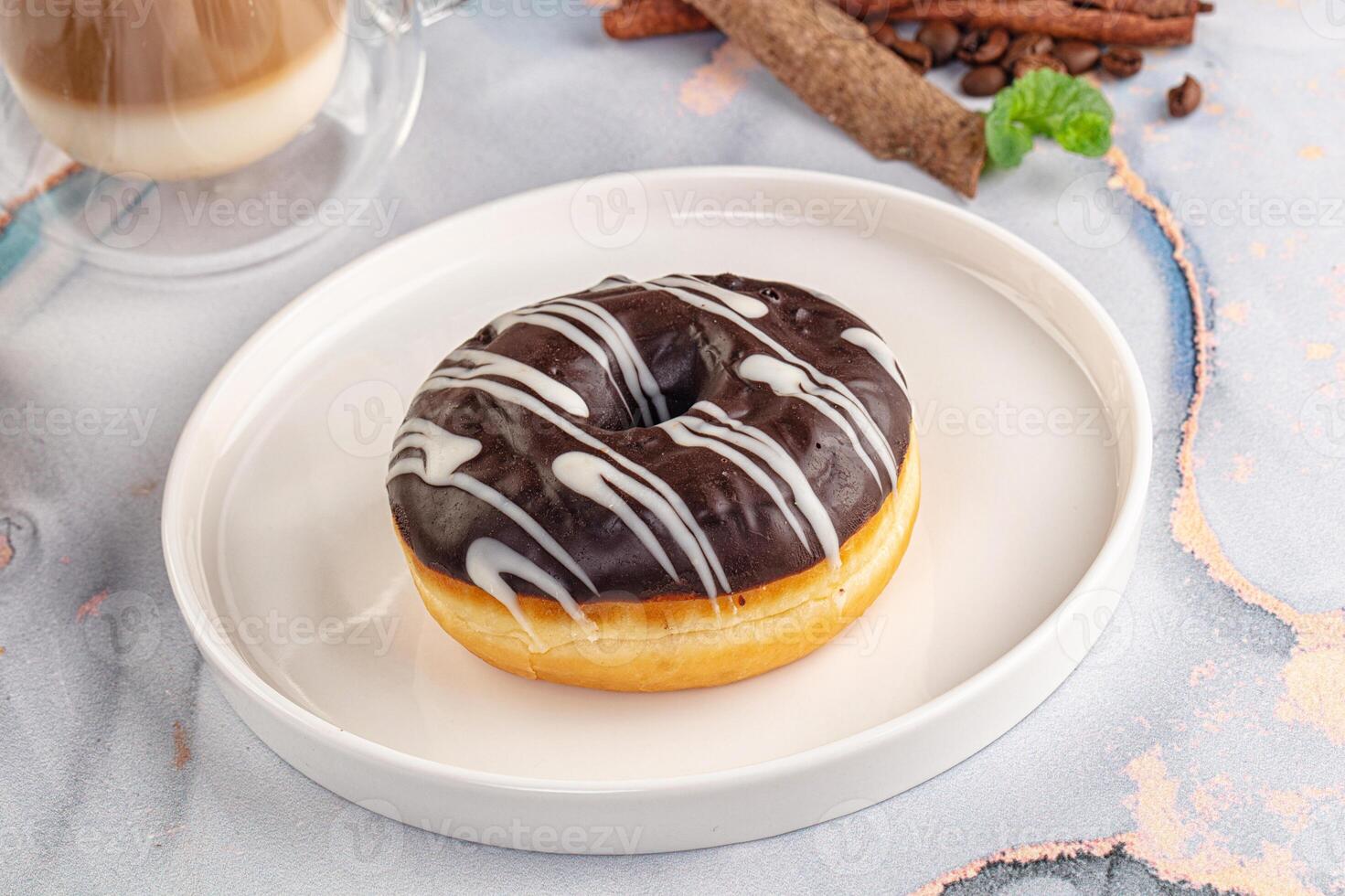 A chocolate glazed doughnut on a white plate with cinnamon and coffee photo