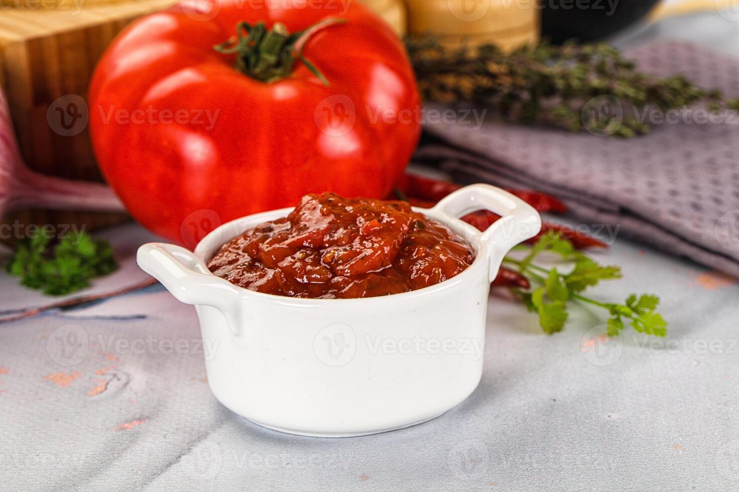 A bowl of chili sauce next to a tomato photo