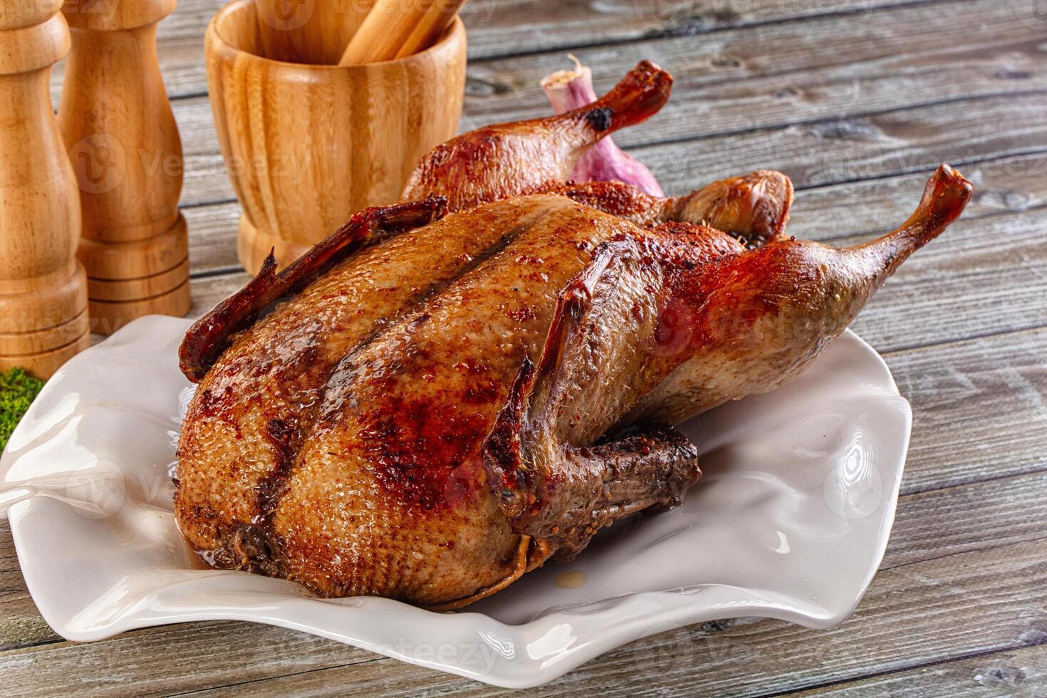 A large roasted duck on a plate with a knife and a wooden spoon photo