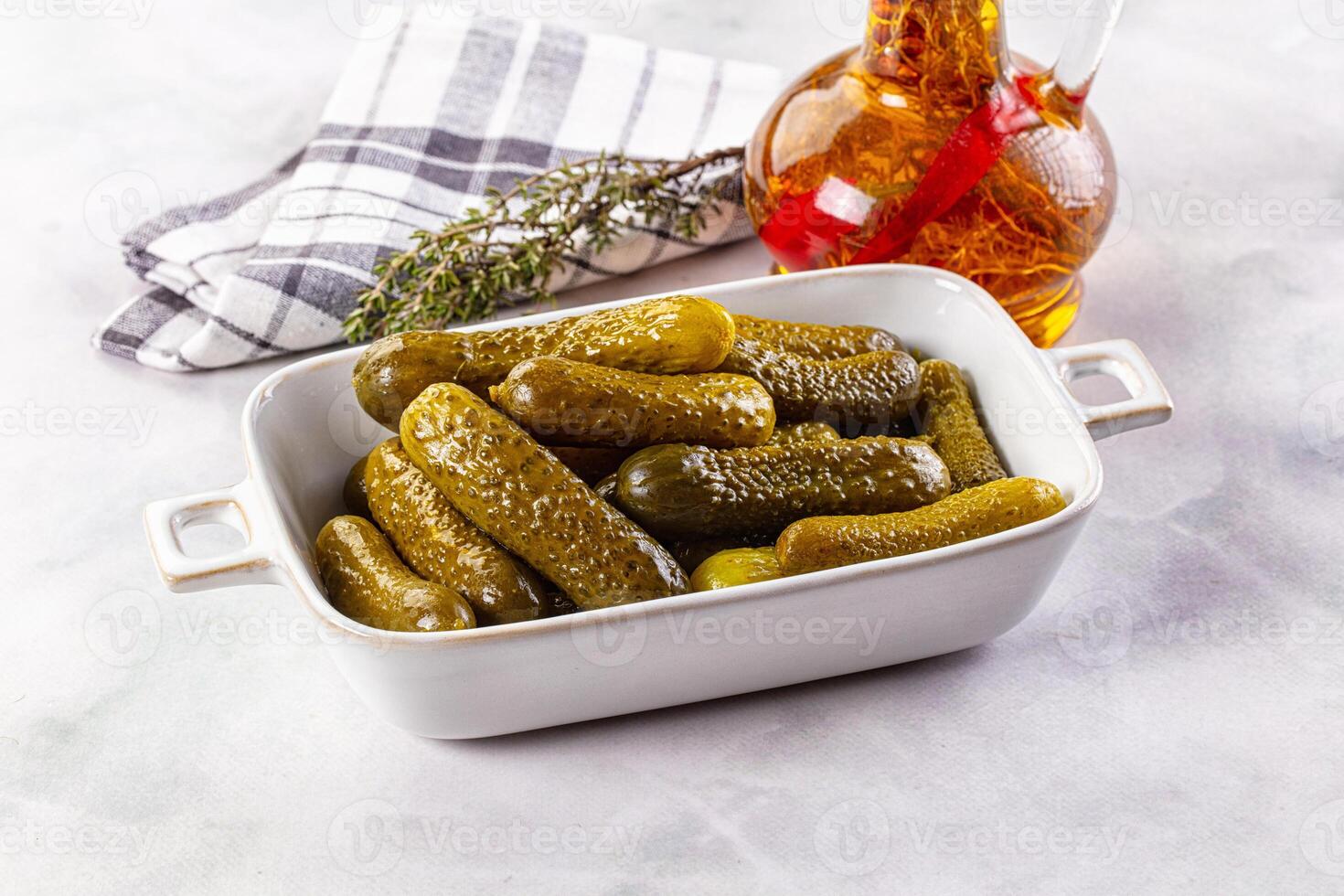 Pickles in a white dish with a bottle of vinegar and a sprig of rosemary photo