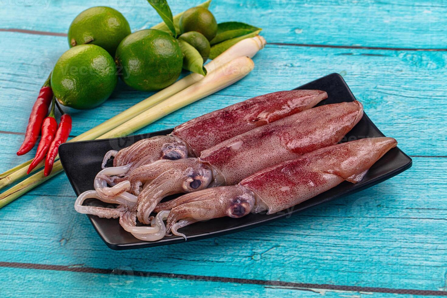 Three squid on a black plate with lime and green onions photo