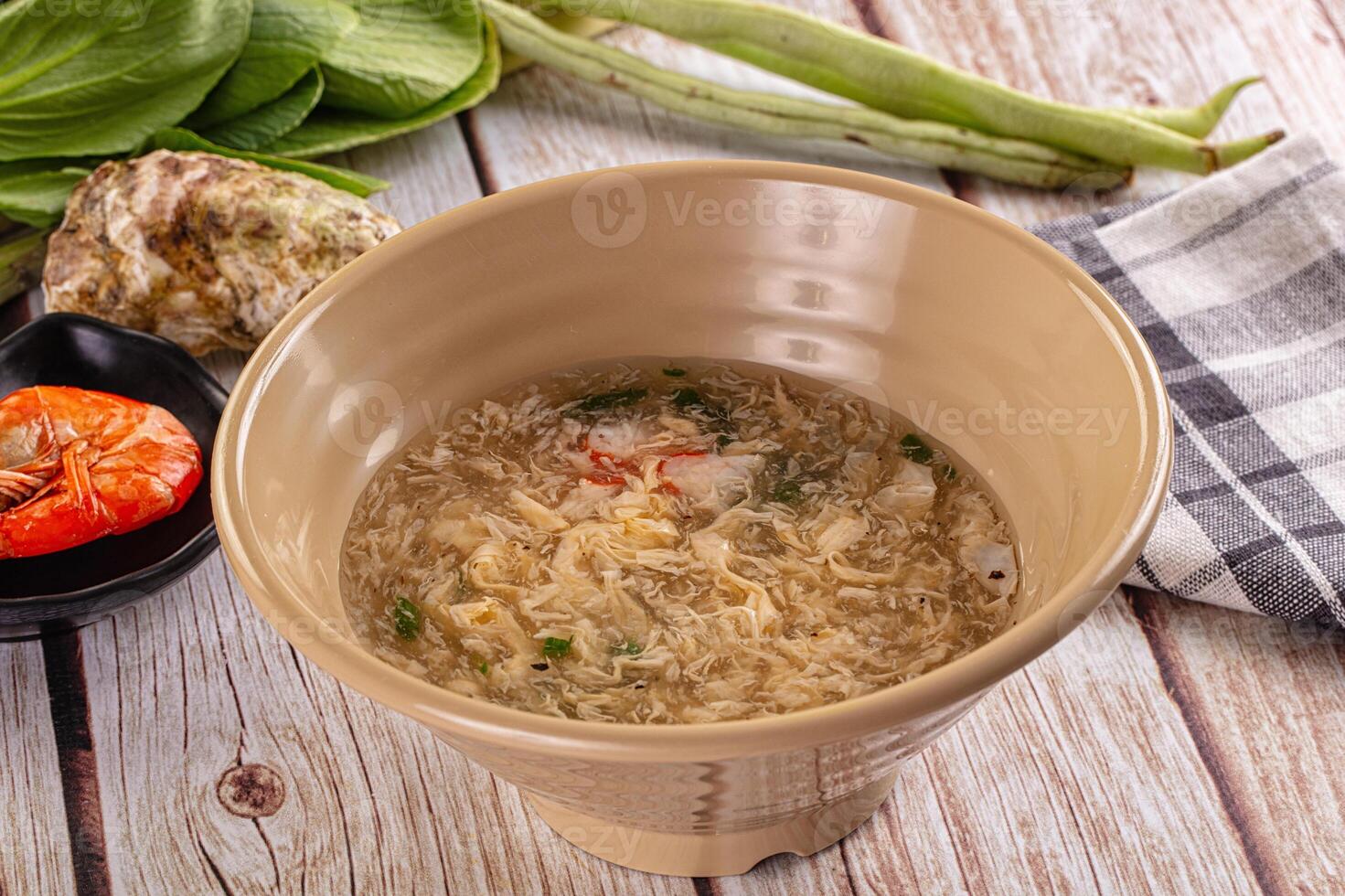 A bowl of soup on a table next to a bowl of vegetables photo