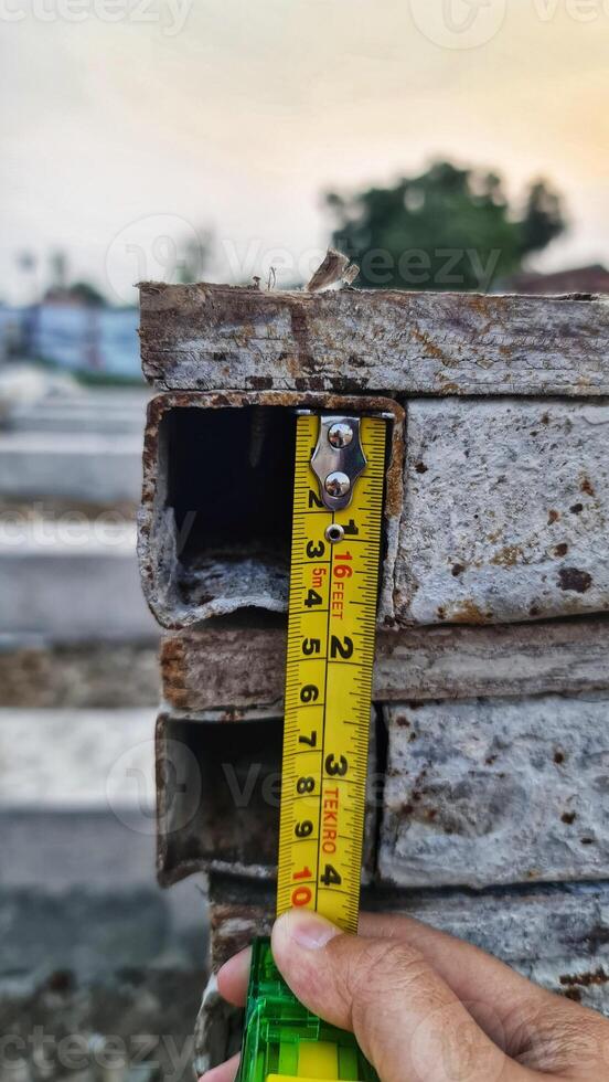 Measuring Rusty Metal Square Tubes with a Yellow Measuring Tape photo