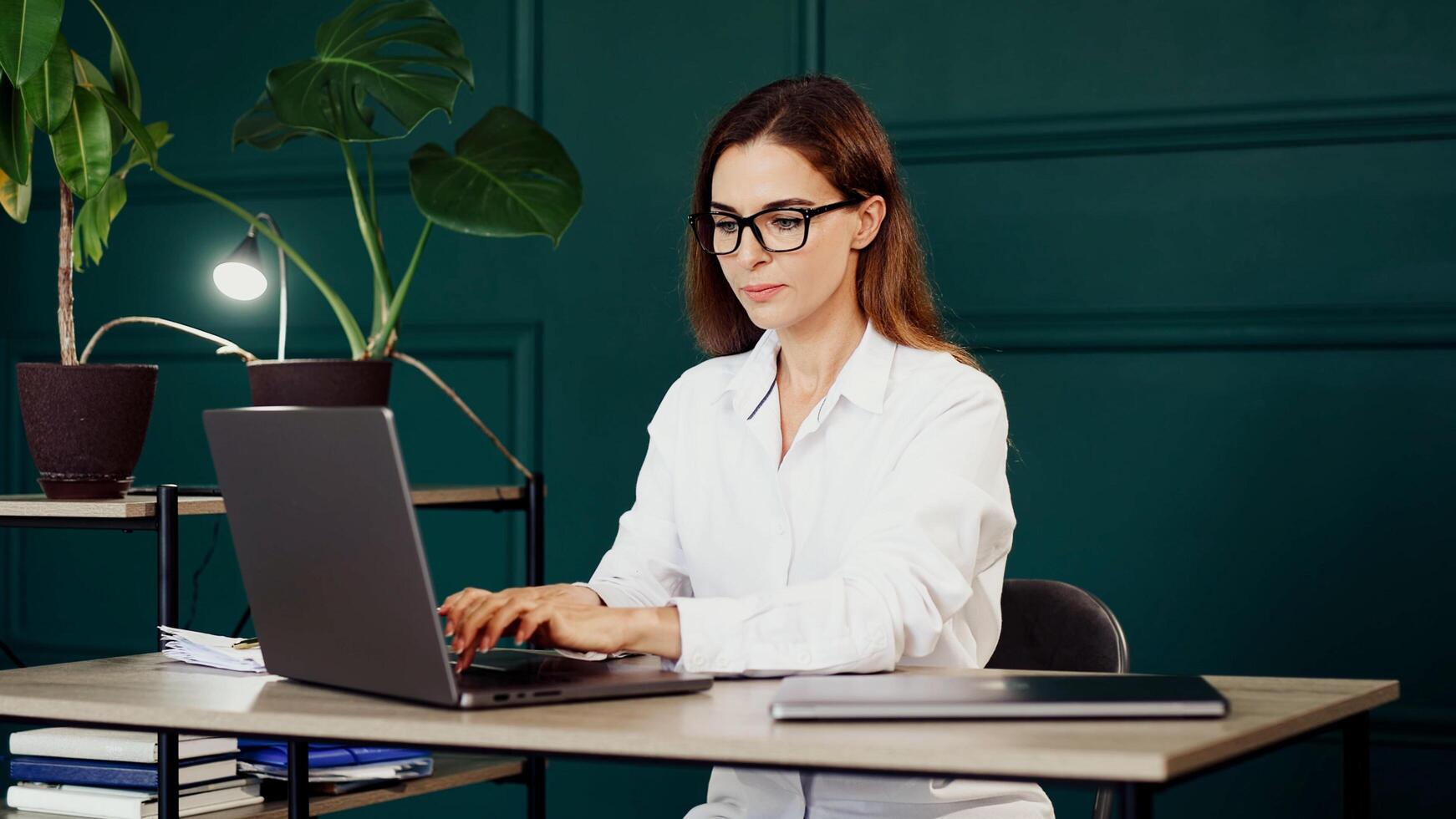 A trendy young woman working on a laptop in a sleek modern office. Ideal for themes of productivity, business success, and contemporary workspaces photo