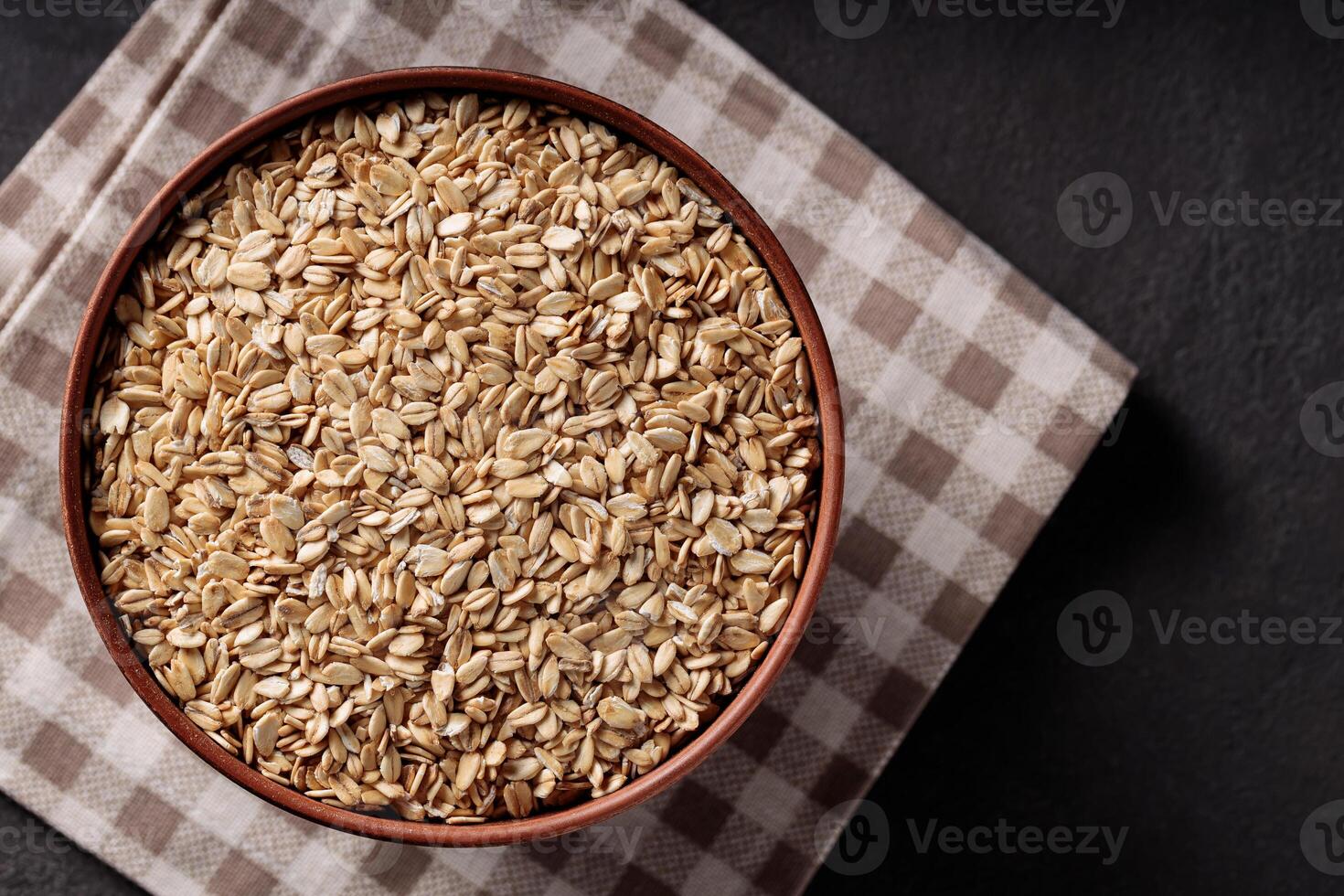 Rolled Oats in Ceramic Bowl on Brown Checkered Napkin Top View photo