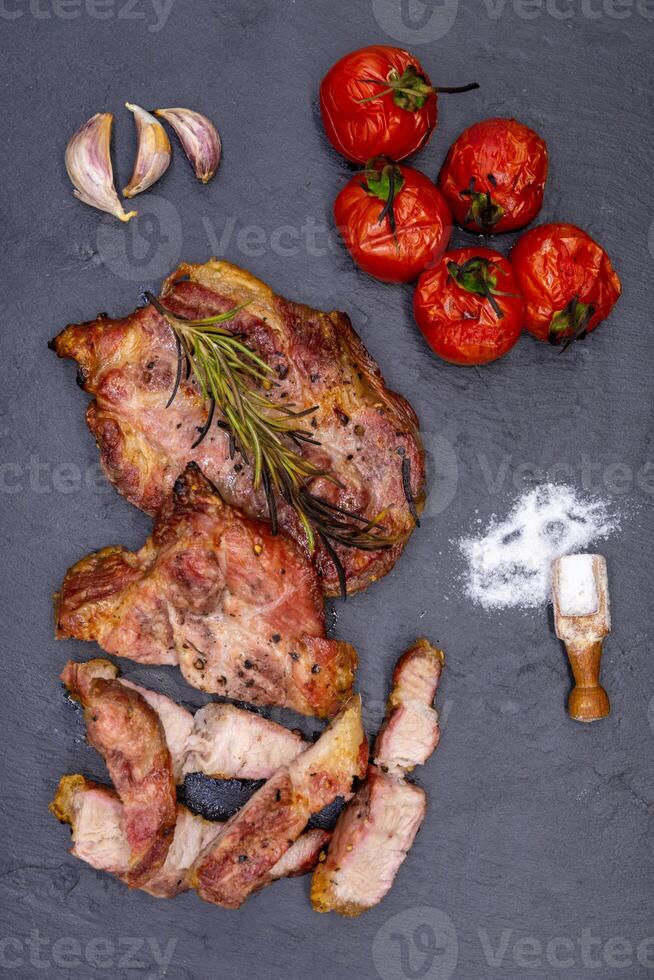 Grilled pork chops with tomatoes and herbs on a slate background photo