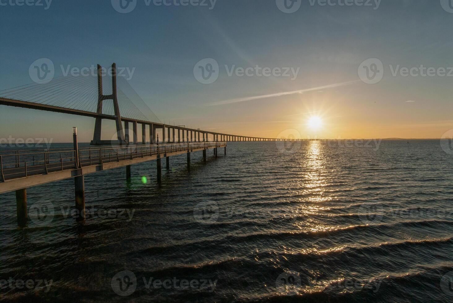 The sun is setting over a bridge over water photo