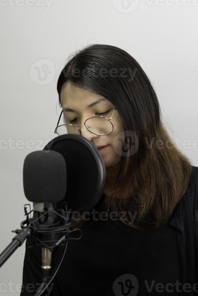 A woman wearing glasses and a black shirt is singing into a microphone photo