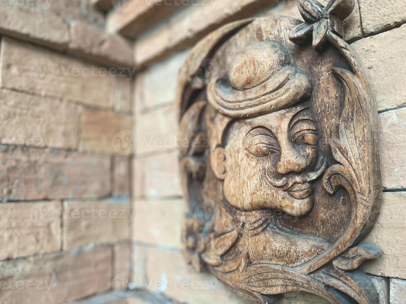 A carved wooden face on a brick wall photo