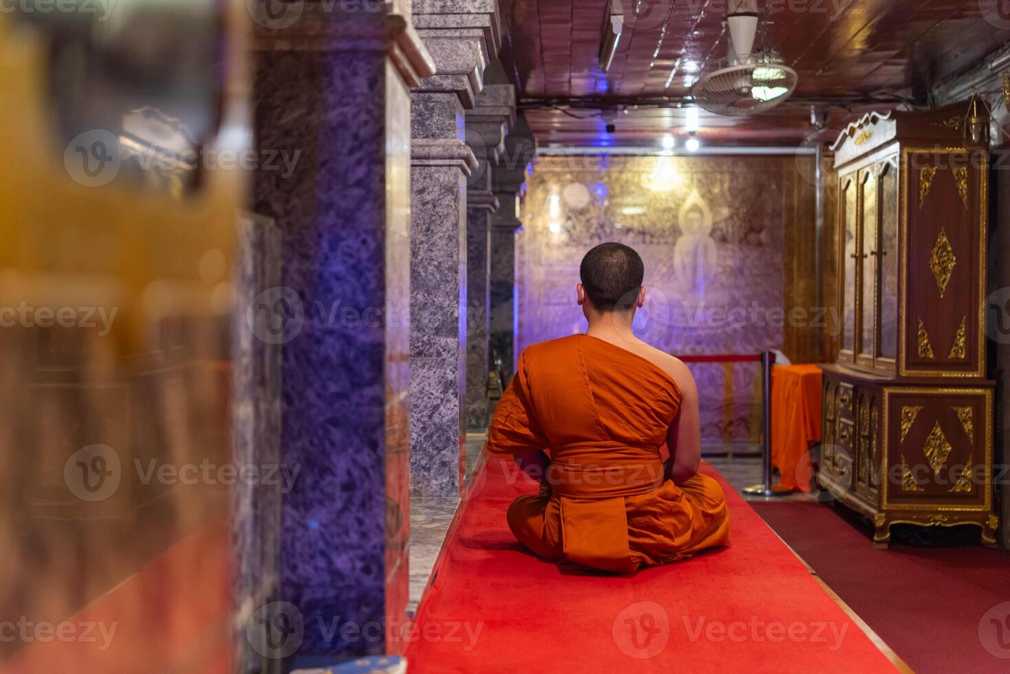 A monk sitting in a temple with a red carpet photo