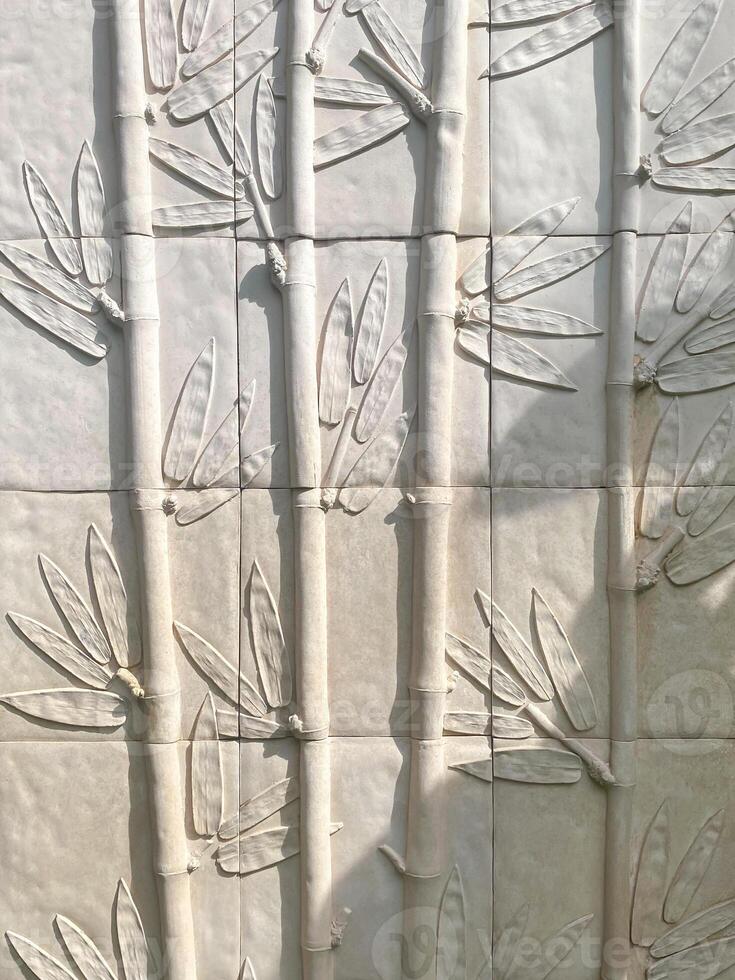A wall with a lot of white tiles with leaves on them photo