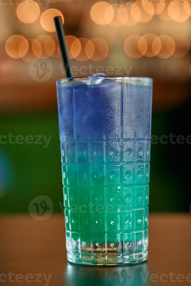 Refreshing blue and green gradient iced drink in a textured glass with straw photo