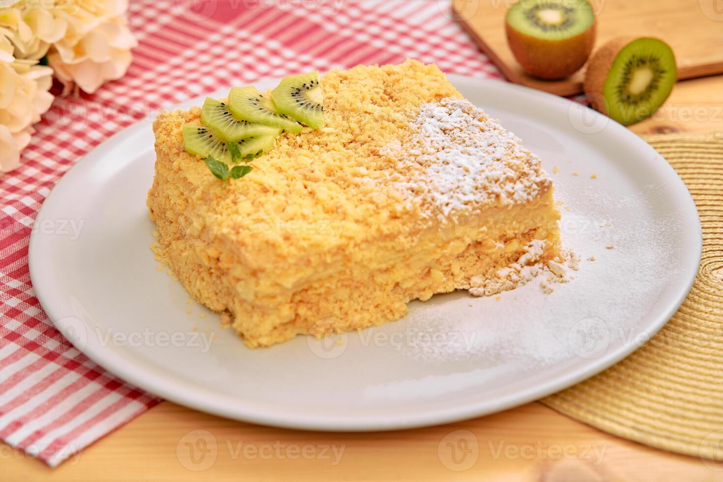Delicious kiwi-topped napoleon cake on white plate with checkered napkin photo