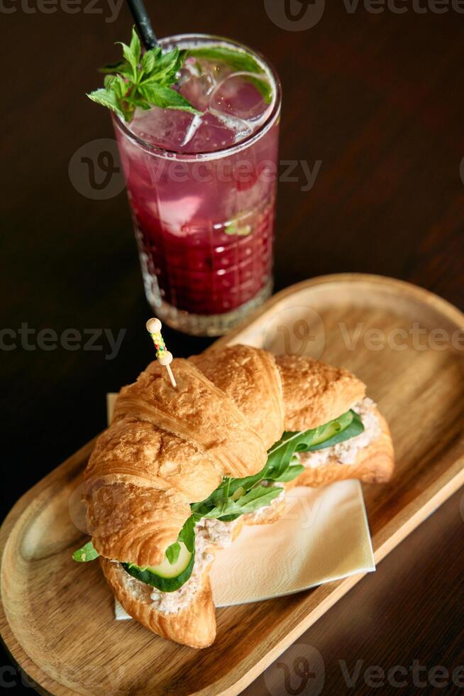 Croissant sandwich and refreshing drink on wooden plate with mint garnish photo