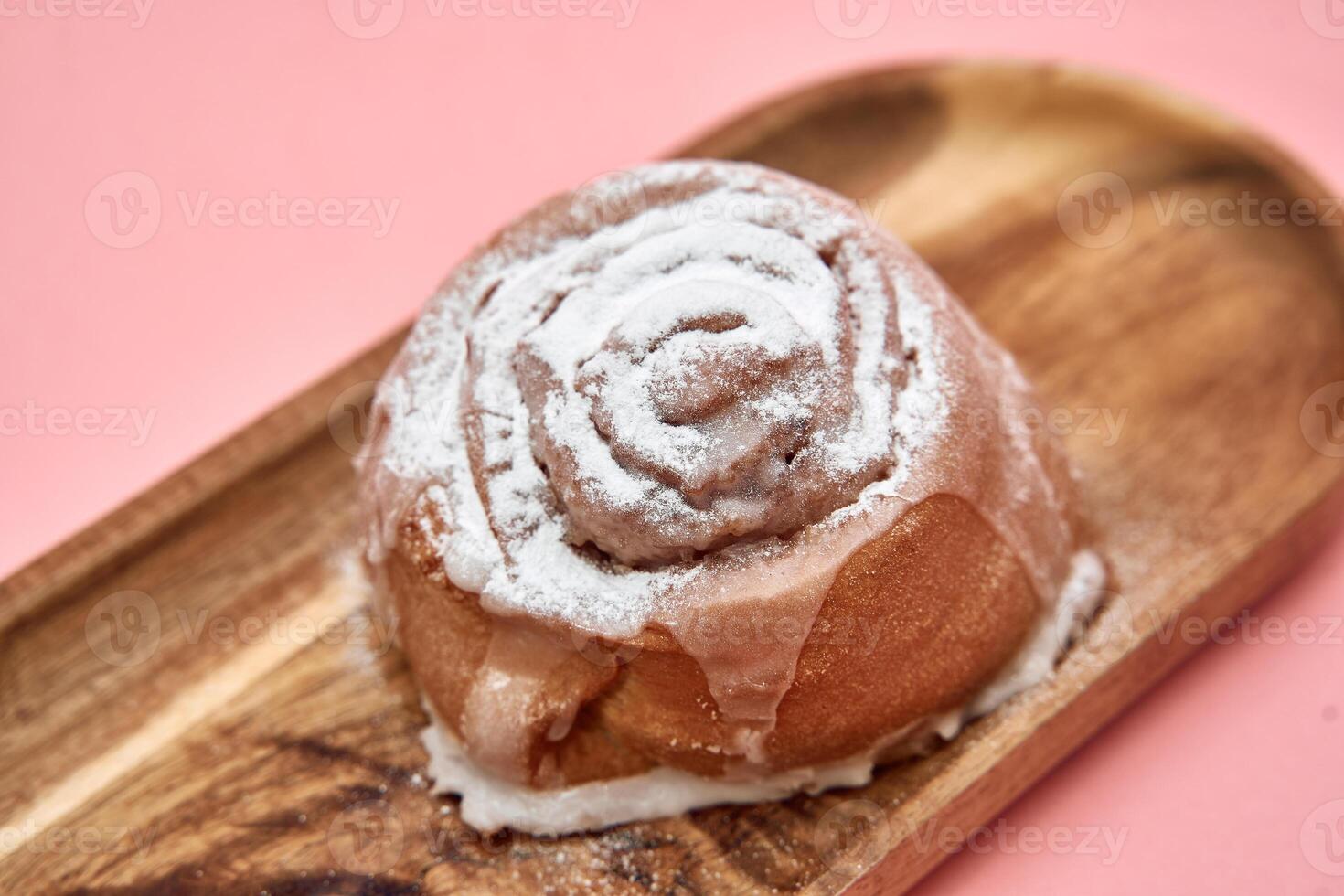 Glazed cinnamon roll on wooden tray with pink background sprinkle of sweetness photo