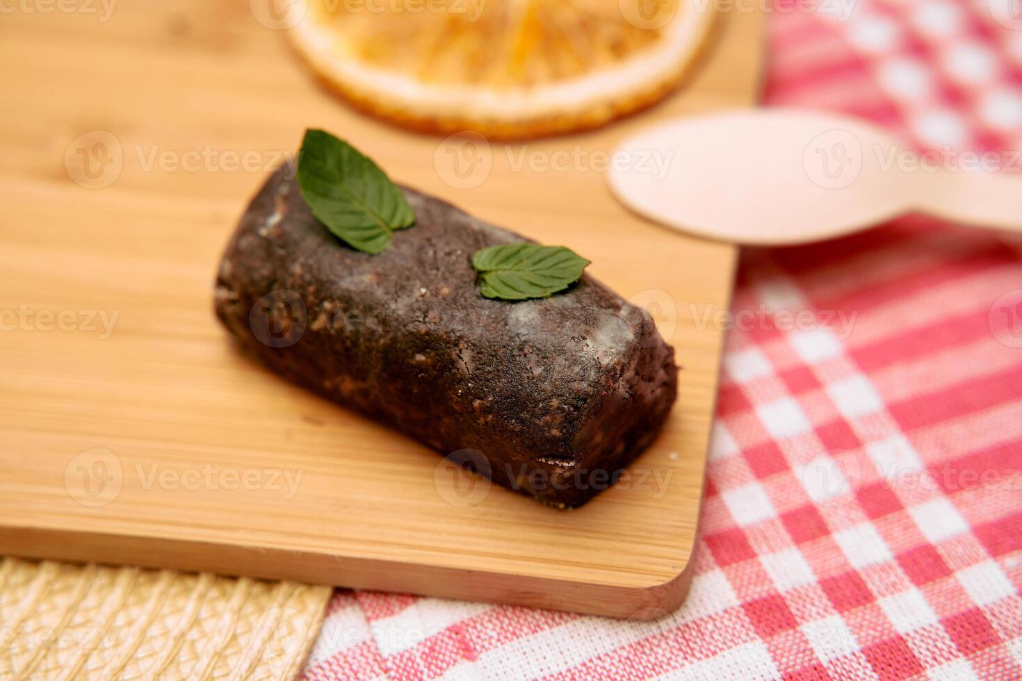 Chocolate ganache log with mint leaves on wooden board with red gingham cloth photo