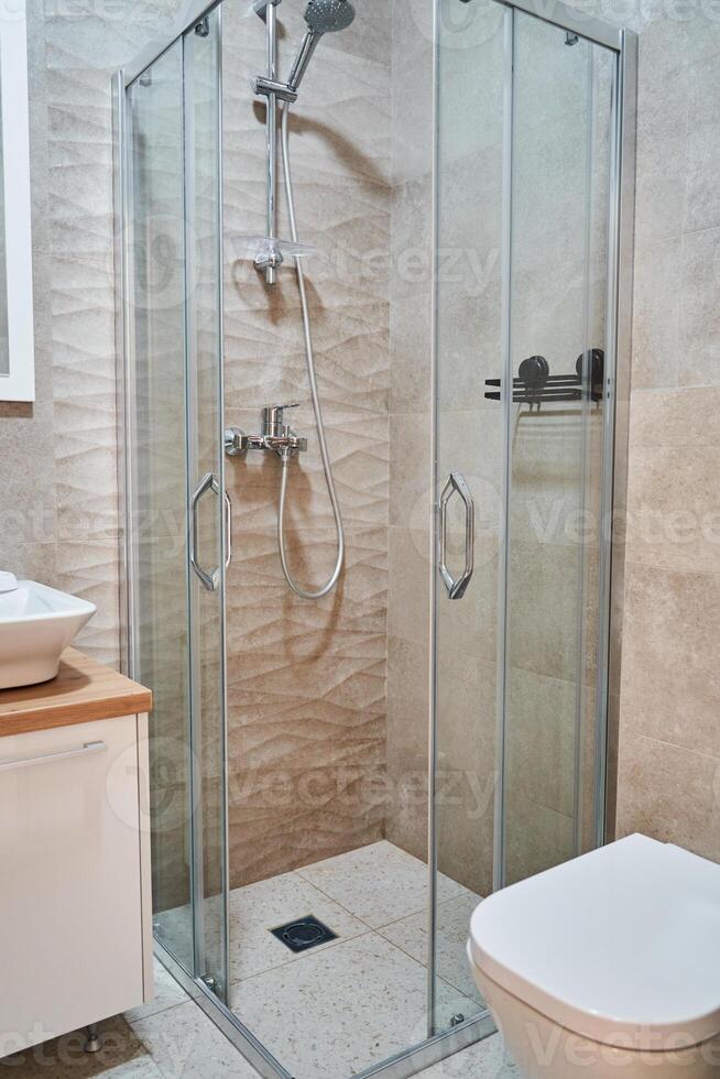 Modern glass shower enclosure in minimalist bathroom with beige tiles photo