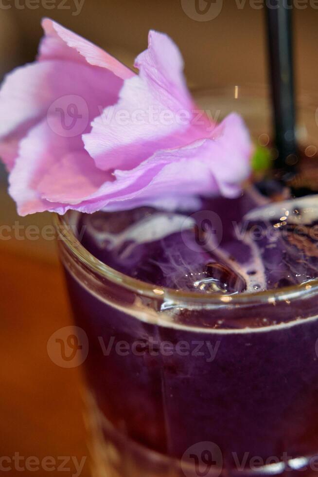 Refreshing purple drink with floral garnish in clear glass with black straw photo