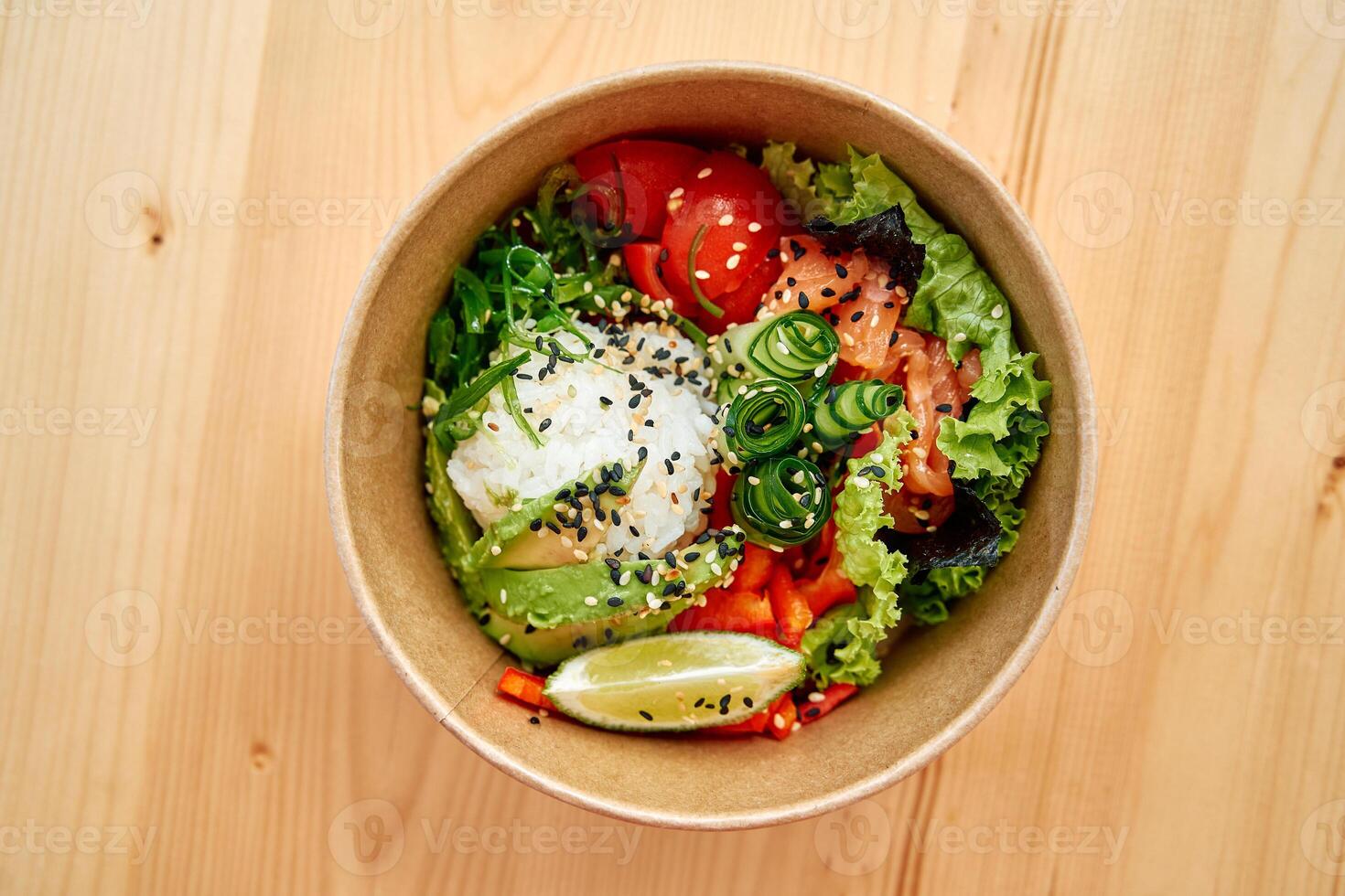 Healthy salmon poke bowl with fresh vegetables, avocado, and lime garnish on wooden table photo