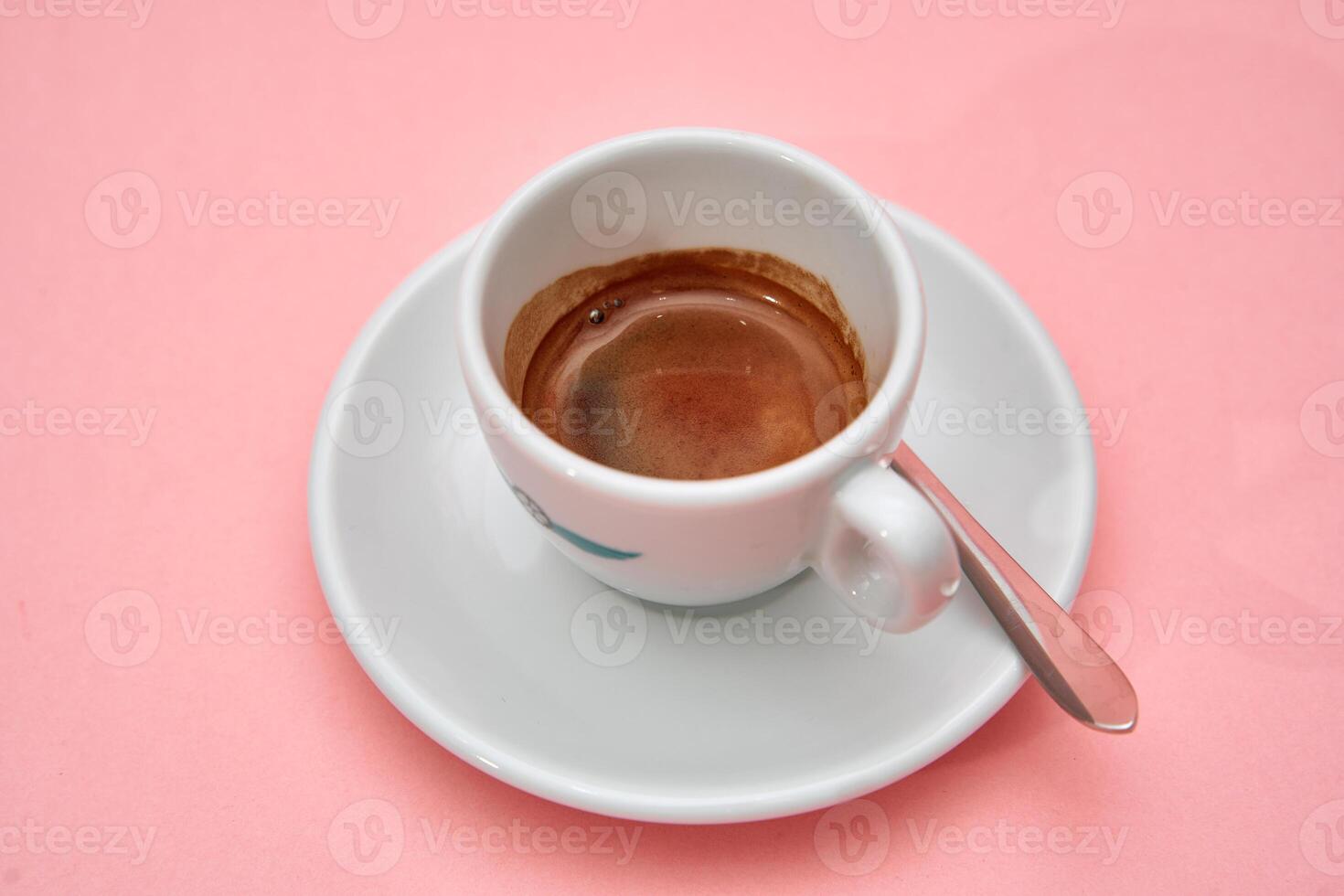 Fresh espresso coffee in white cup on pink background with silver spoon photo