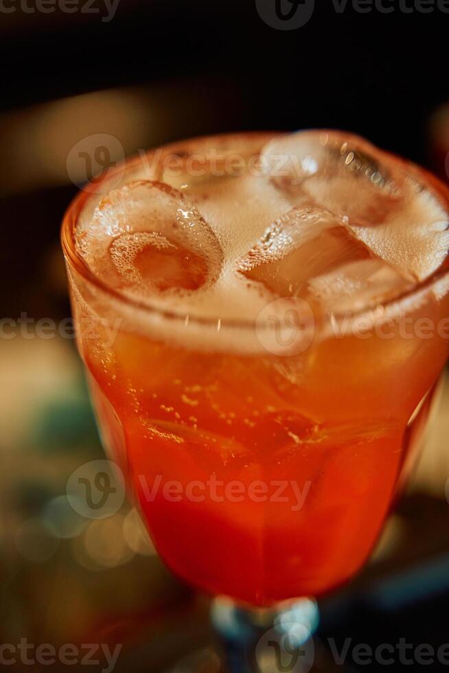 Refreshing orange cocktail in glass with ice cubes on a dark background photo