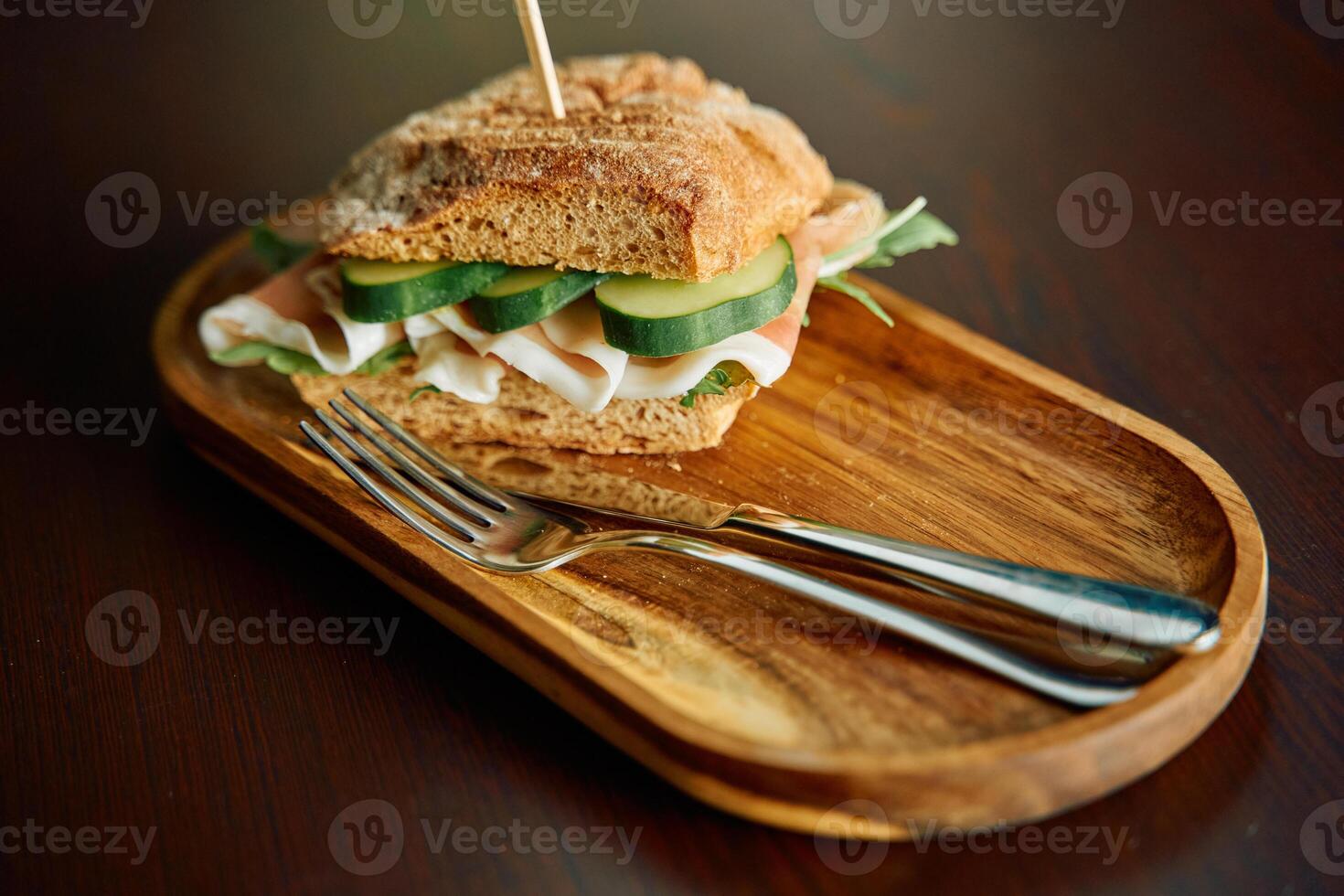 Gourmet turkey sandwich on wooden plate with fresh vegetables and arugula photo