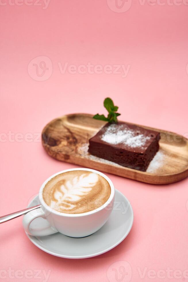 Cappuccino with latte art and chocolate cake on wooden tray against pink background photo