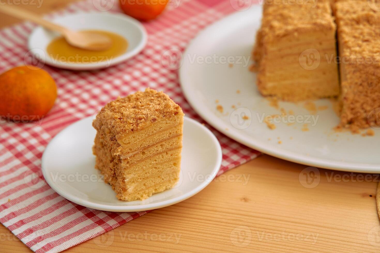 Layered honey cake with crumb topping on red checkered cloth featuring whole mandarin oranges photo