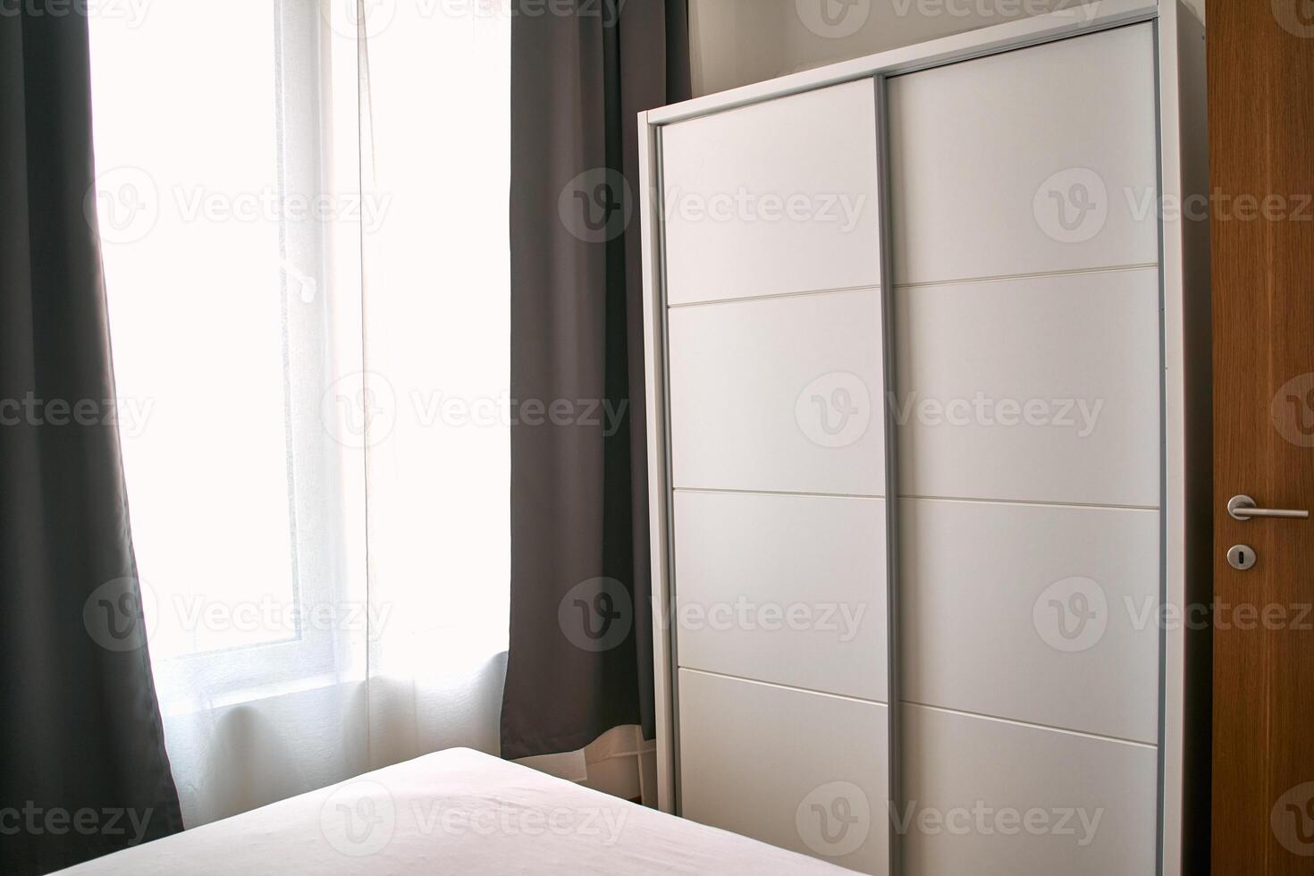 Minimalist bedroom wardrobe with white sliding doors next to curtain-filtered sunlight for modern interior design photo