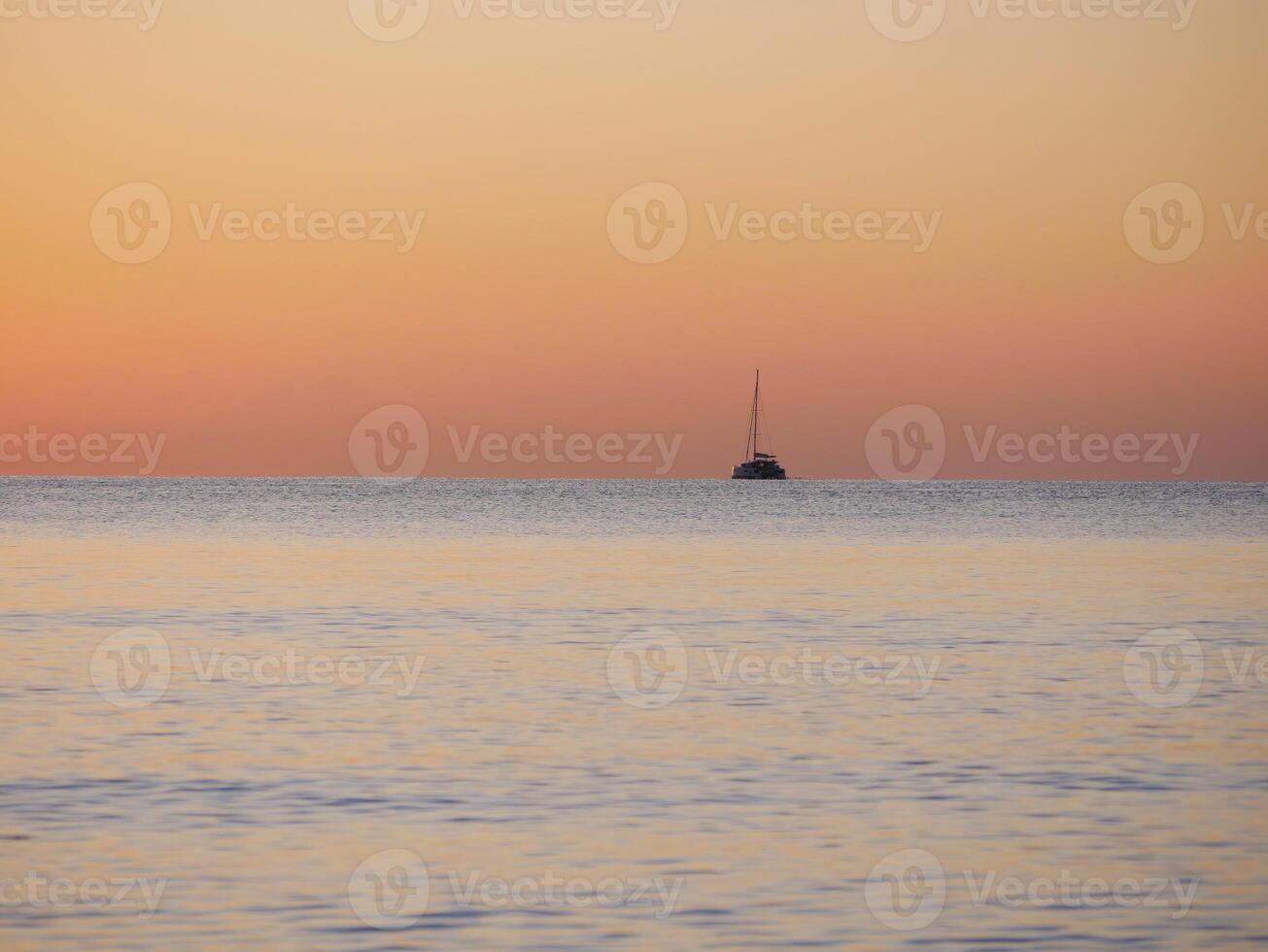 A breathtaking sunset over the calm sea with a sailboat on the horizon. Warm orange and golden tones fill the sky and reflect on the water. Travel, nature, relaxation, and maritime concept photo